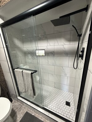 Een douche met glazen wand, betegelde vloer en een handdoekhouder.