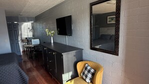 Quarto compacto com cozinha compacta, uma cama, uma poltrona amarela e uma TV de tela plana fixada na parede.
