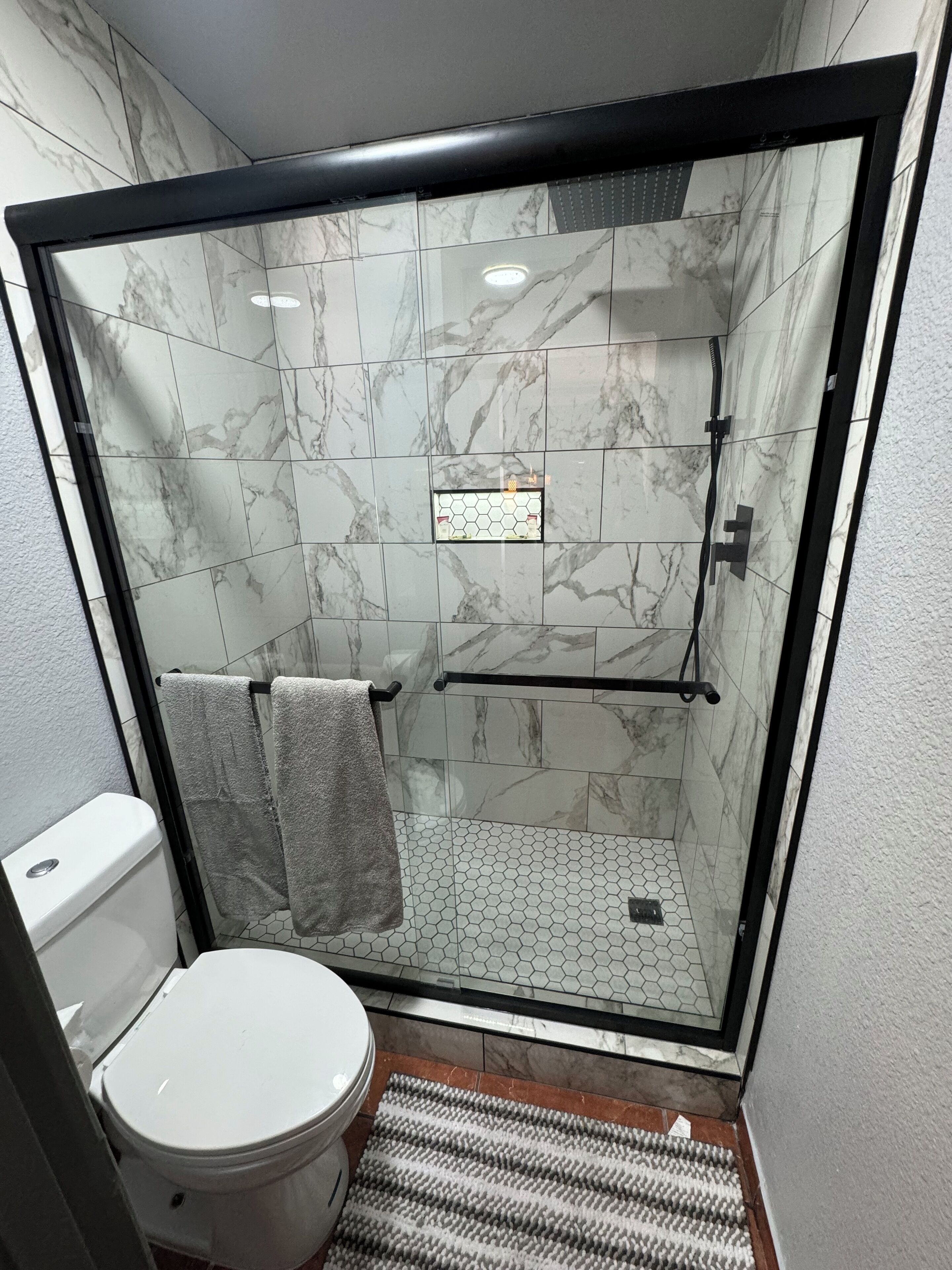 Ein Badezimmer mit Duschkabine, Toilette und Fliesenboden mit Sechseckfliesen.