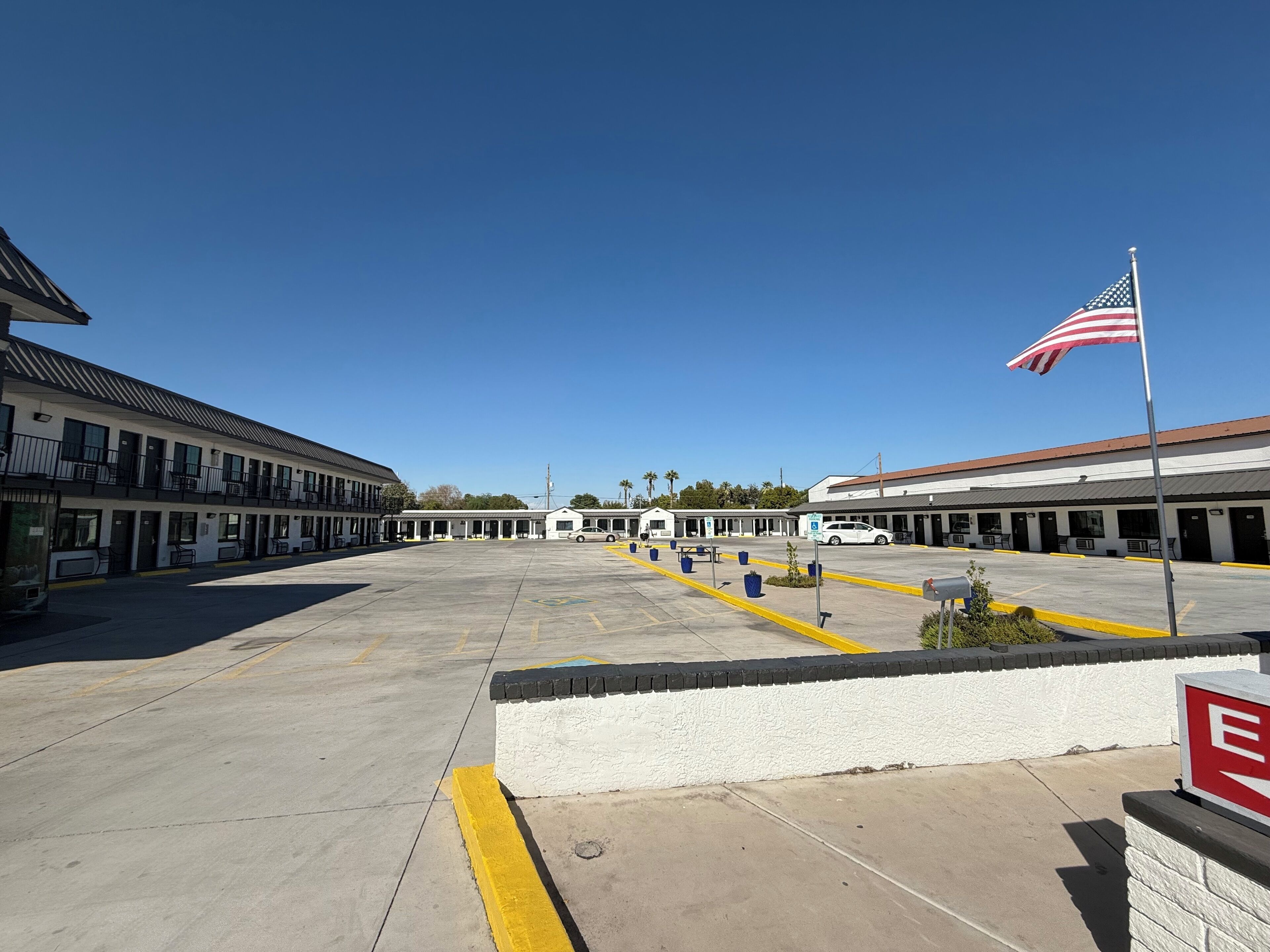 A motel with a parking lot, a row of rooms, and an American flag.