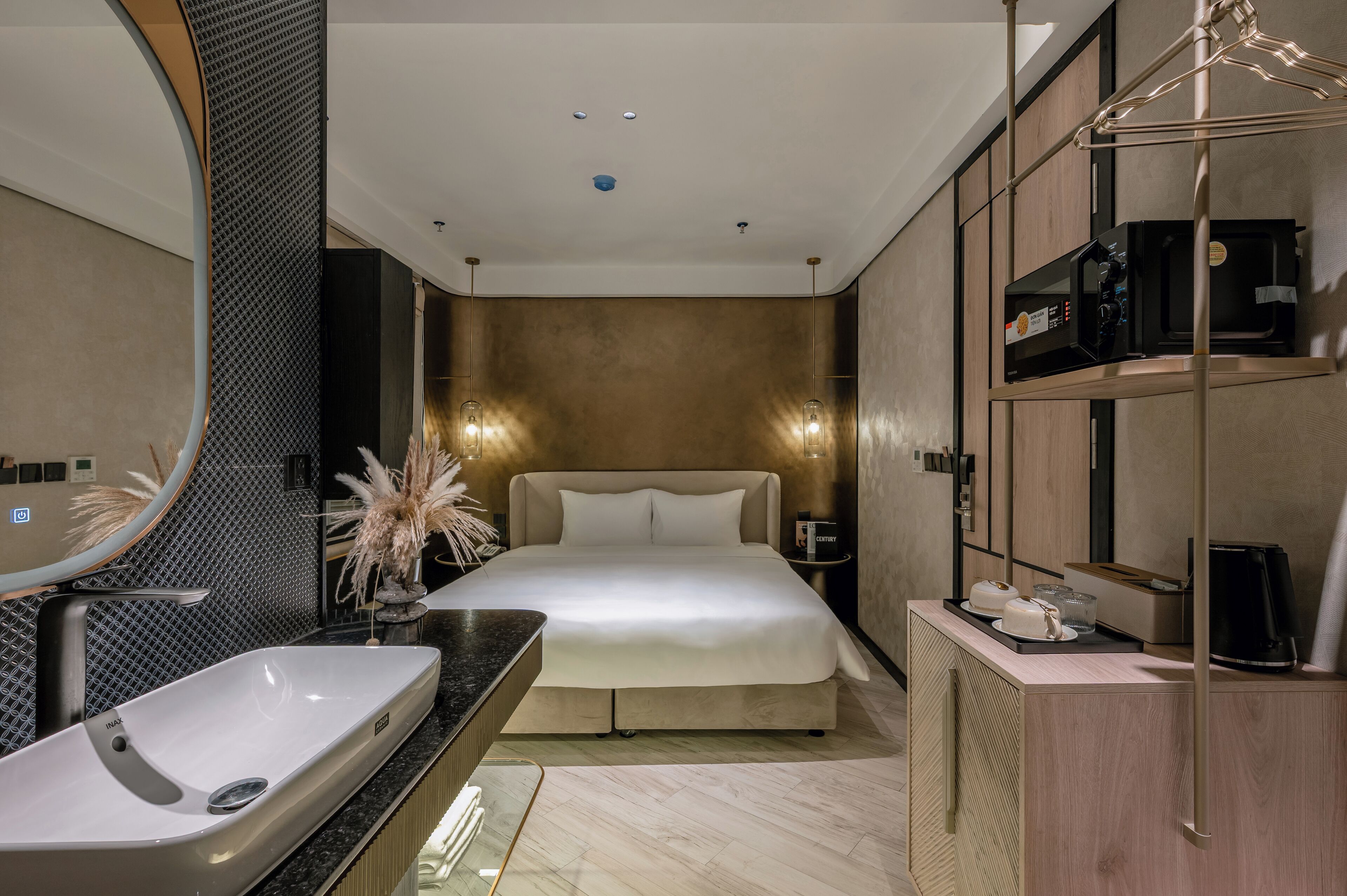 A modern hotel room with a large bed, a built-in vanity with a sink, a large mirror, and a minibar.
