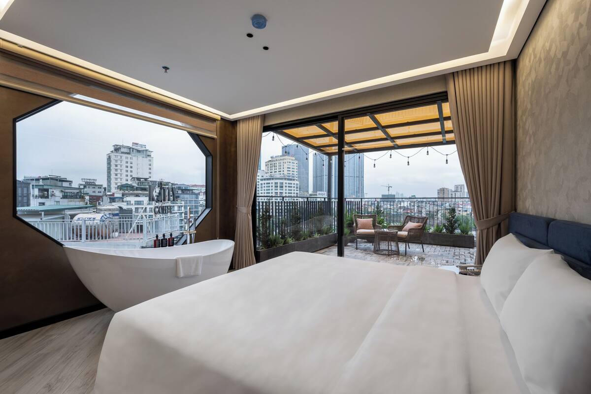 A modern hotel room with a large bed, a bathtub, and a balcony with a city view.