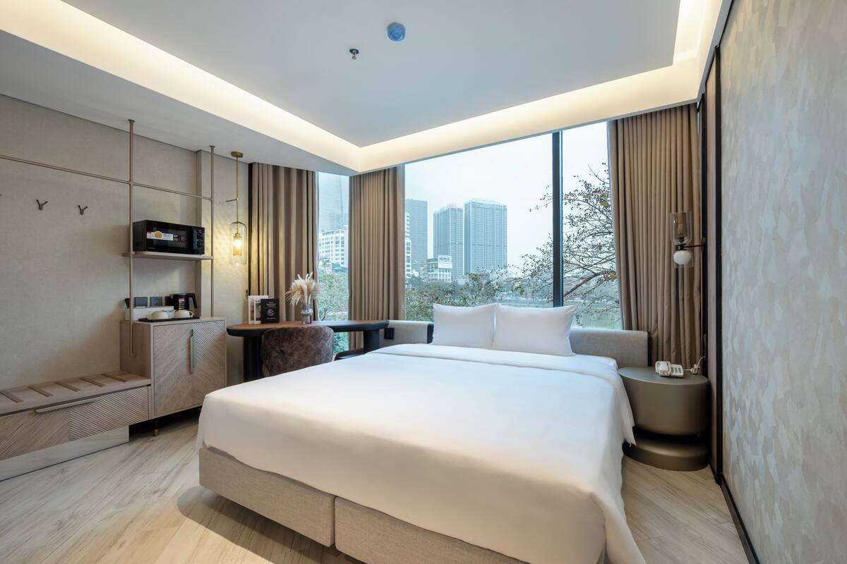 A modern hotel room with a large bed, a desk with a computer, a TV, and a view of the city.
