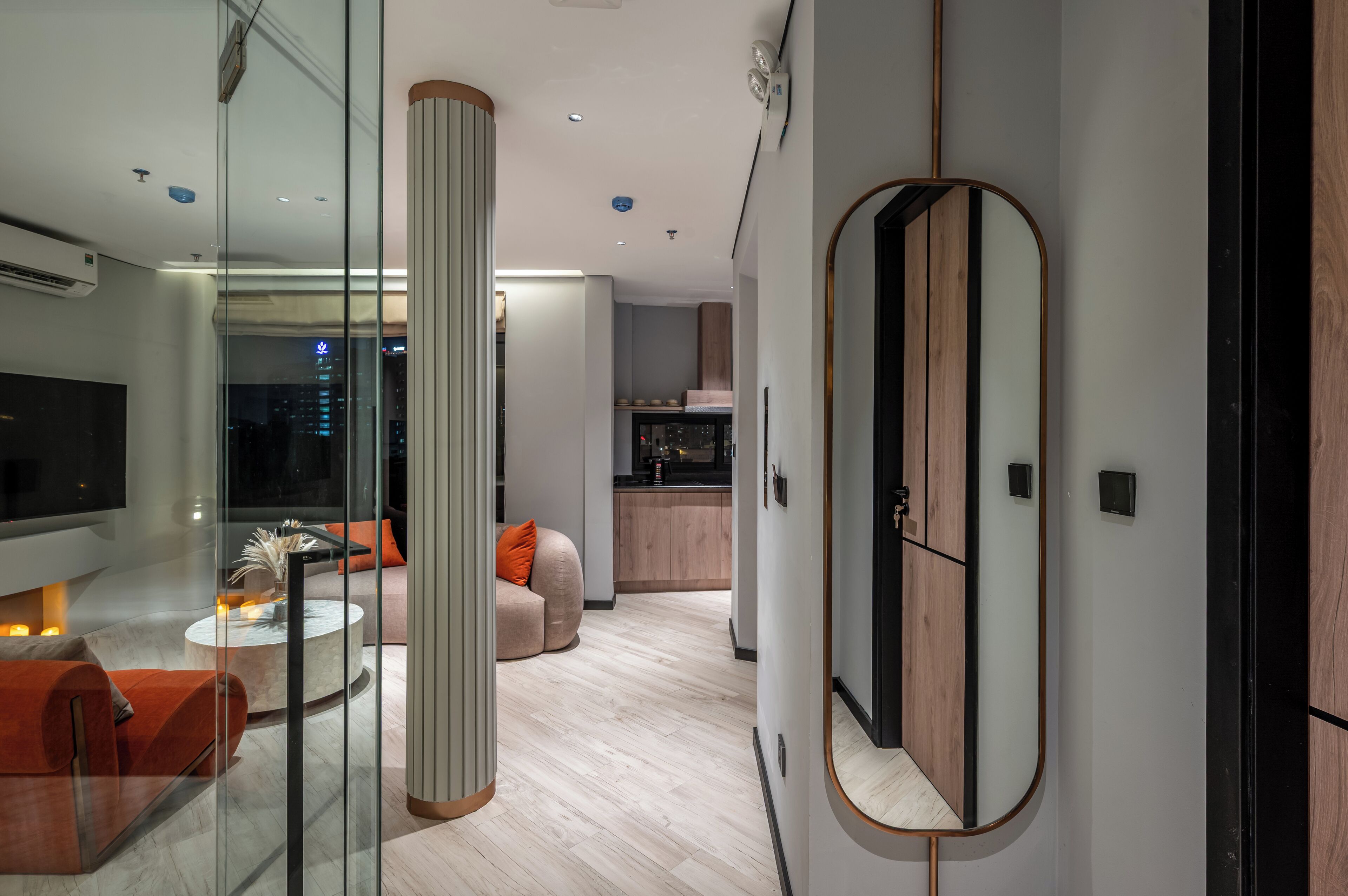 Un salon moderne avec une cloison en verre, une table basse ronde et un canapé. On aperçoit un coin cuisine à l’arrière-plan.