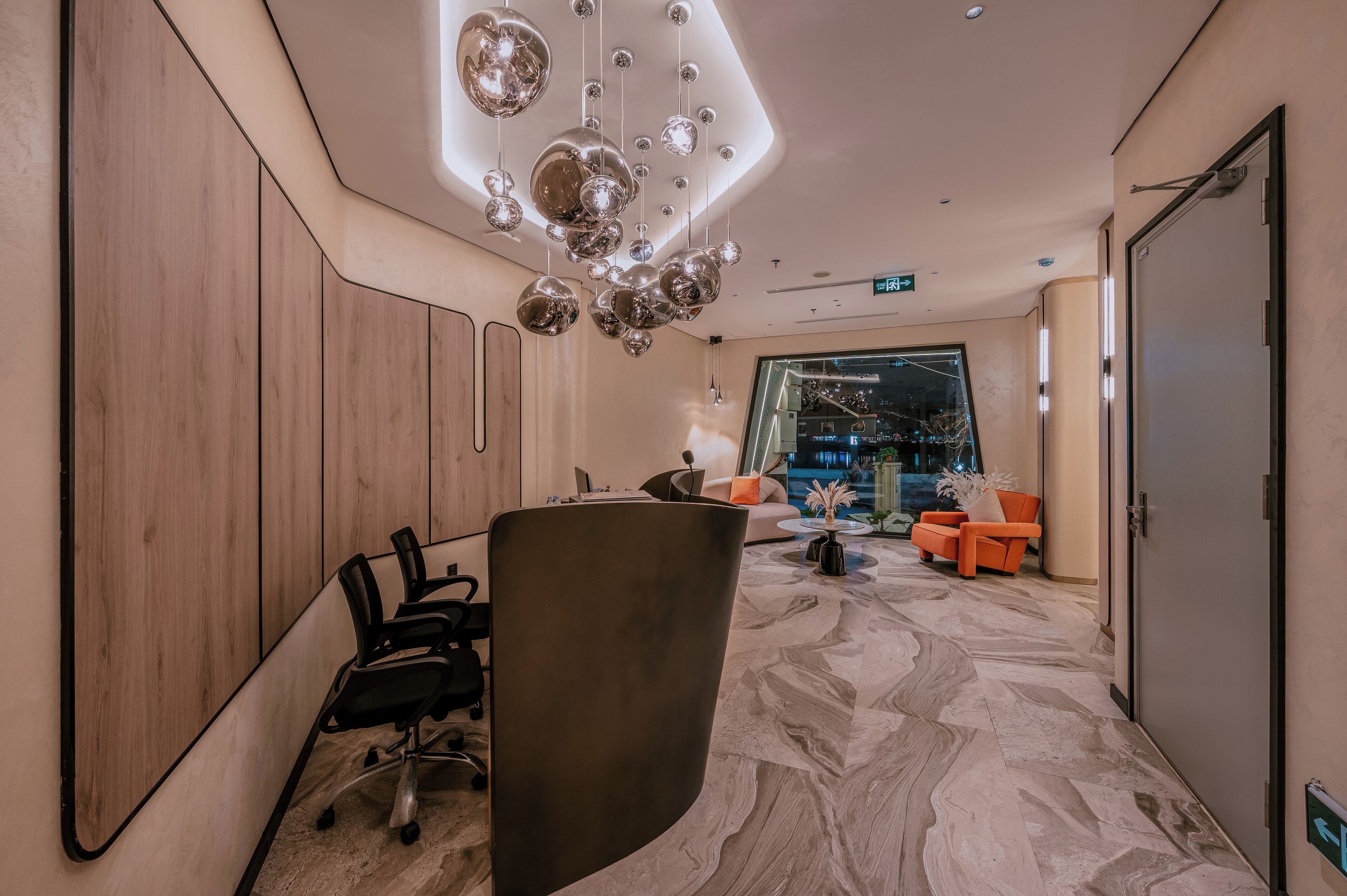 Un espace d’accueil moderne avec un comptoir incurvé, des chaises de bureau noires et un coin salon avec des chaises orange.