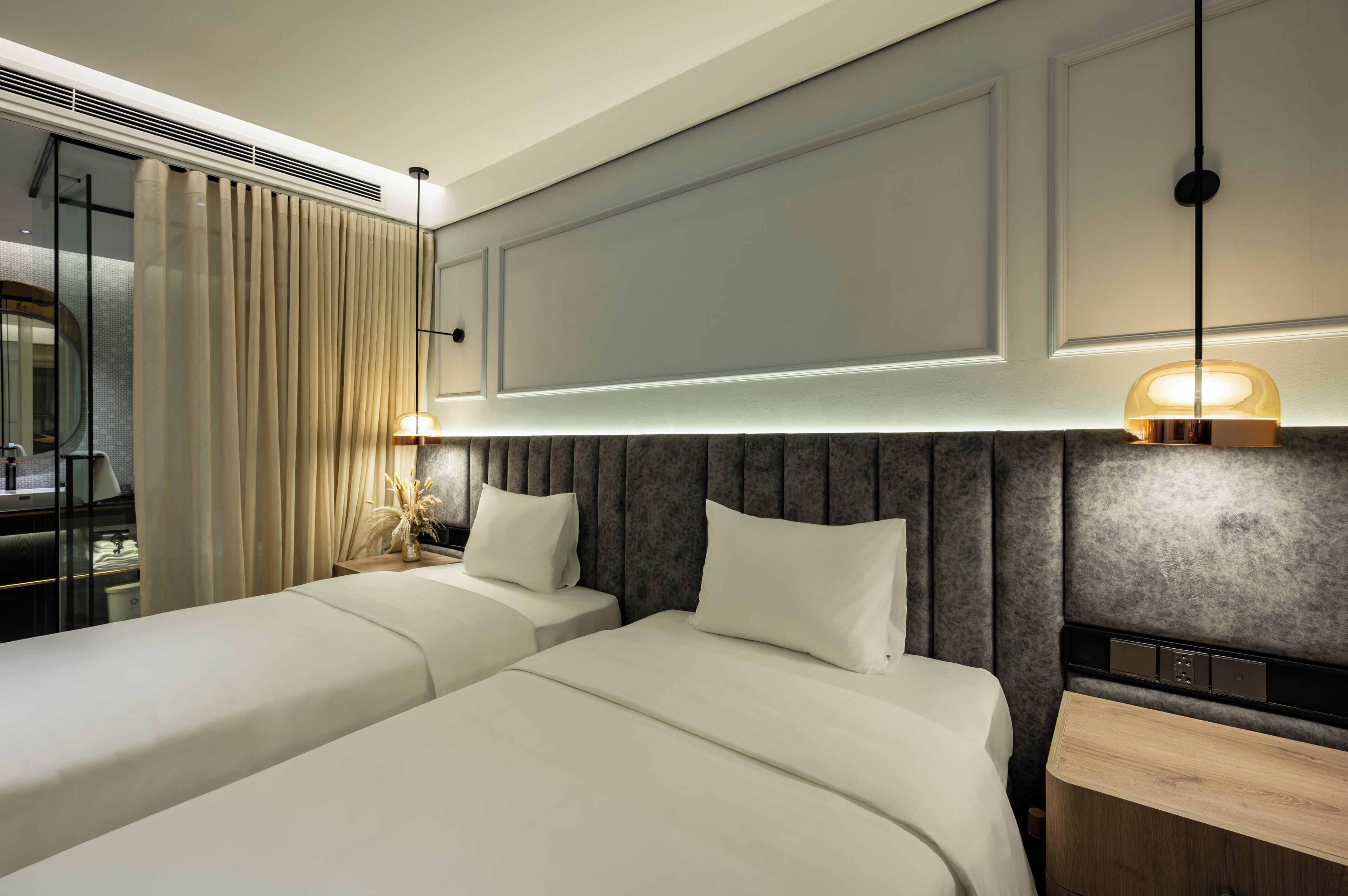 A modern hotel room with two beds, a large mirror, and a nightstand with a lamp.