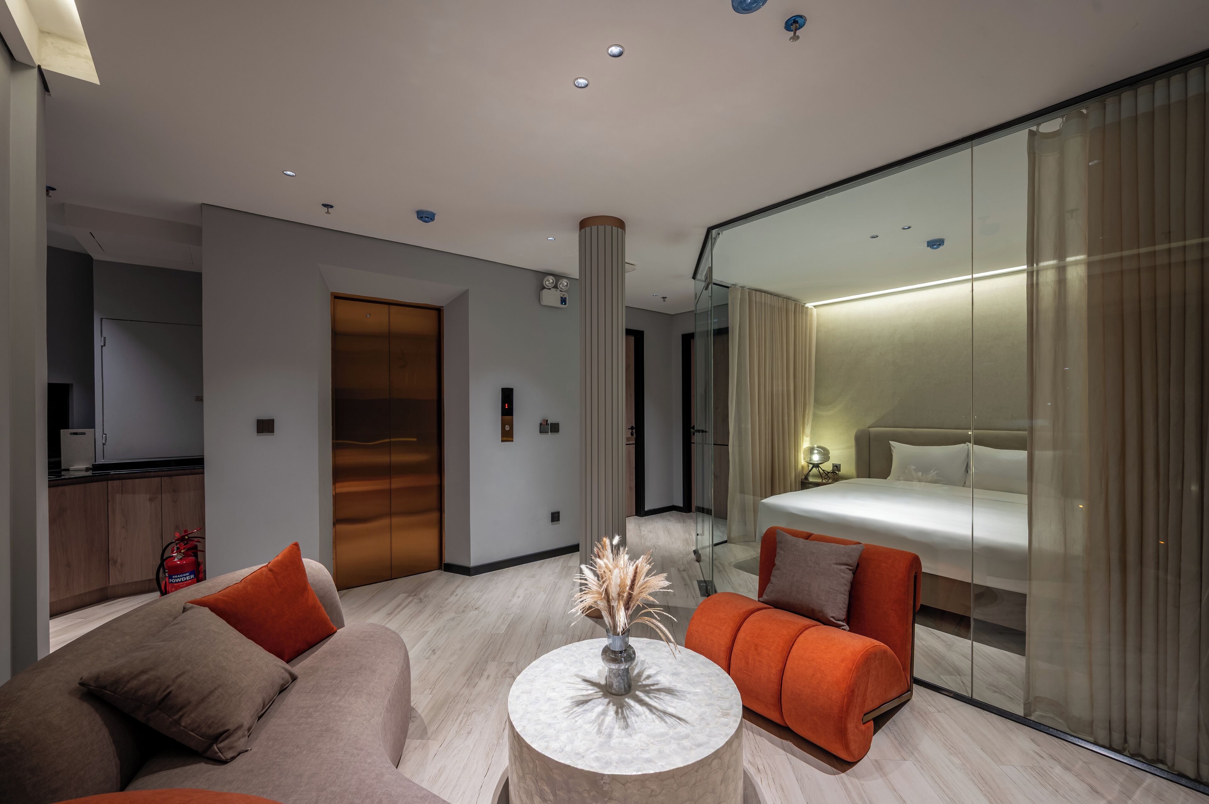 A modern hotel room with a large bed, a sofa, a coffee table, and a glass partition.