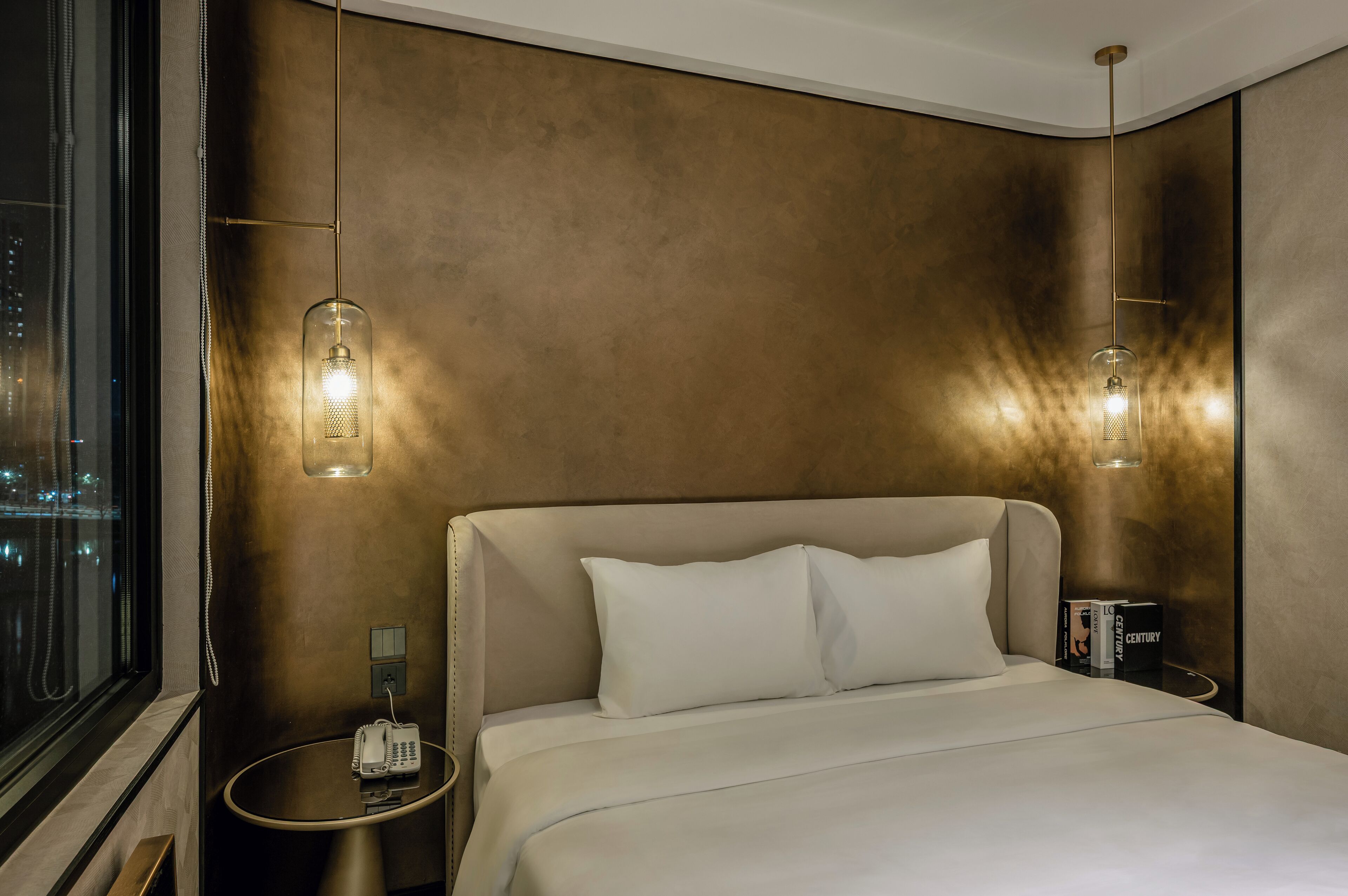 A modern hotel room with a large bed, two bedside tables, a telephone, and two pendant lights.