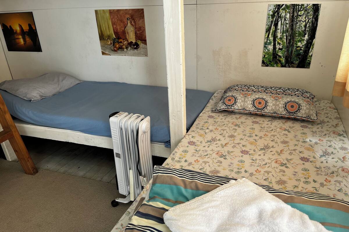 Ein kleines Zimmer mit einem Einzelbett, einem Heizkörper, einer blauen Matratze und einer zudeckenden Bettwäsche mit Blumenmuster.