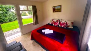 A bedroom with a large bed, a painting on the wall, and a view of a garden through a sliding door. - Taringatura Backpackers (Dipton West)