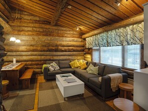 L'intérieur d'une cabane en rondins, avec un canapé, une table basse et une fenêtre équipée de stores.