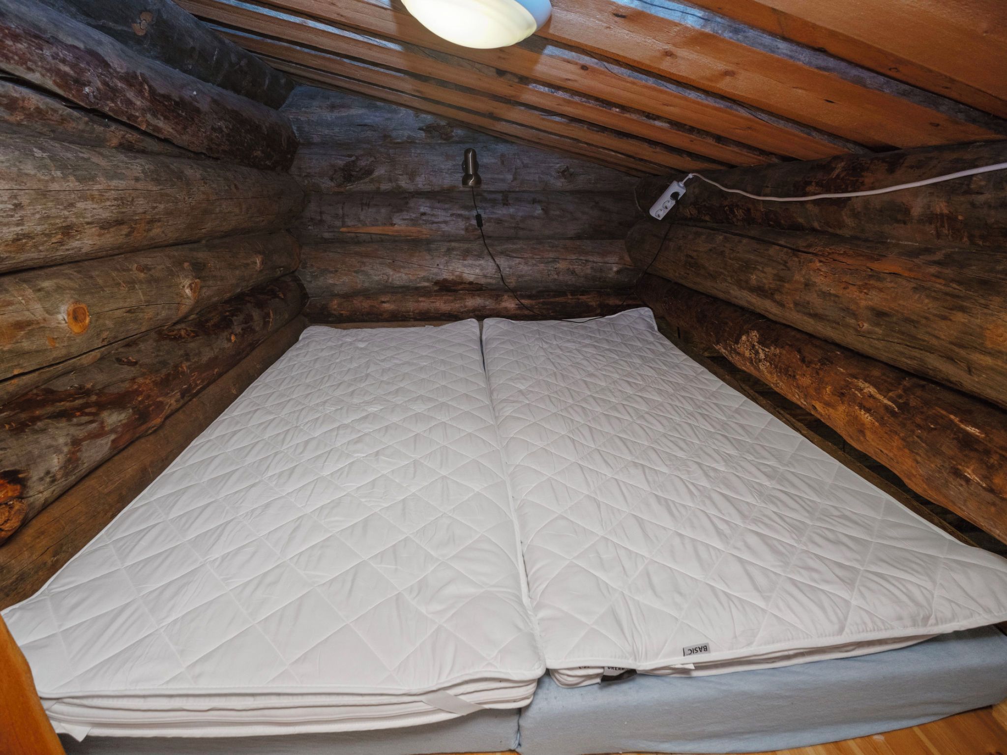 A log cabin room with a mattress and a power outlet on the wall.