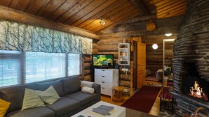 Acogedor interior de cabaña de madera con sala de estar que incluye un sofá, un televisor, una chimenea y una pared de piedra.