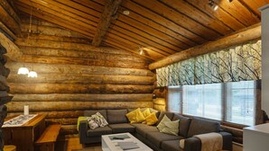 Interior de una cabaña de troncos con sofá, mesa de centro y muebles de madera.