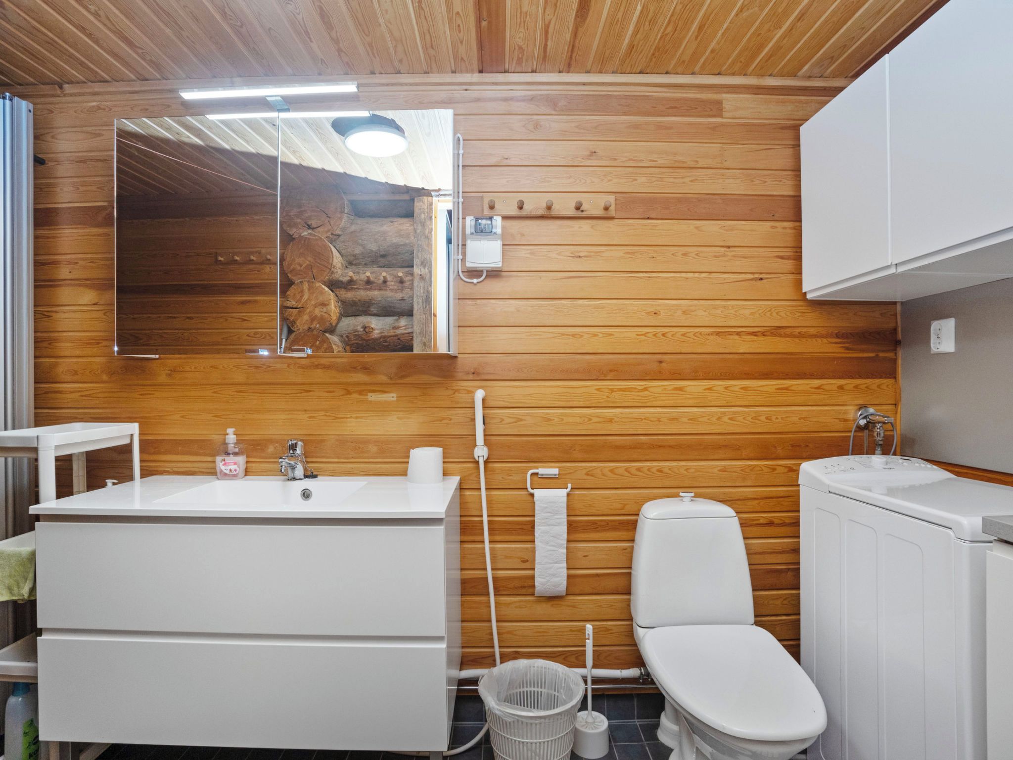 A bathroom with a wooden wall, a sink, a toilet, and a mirror.