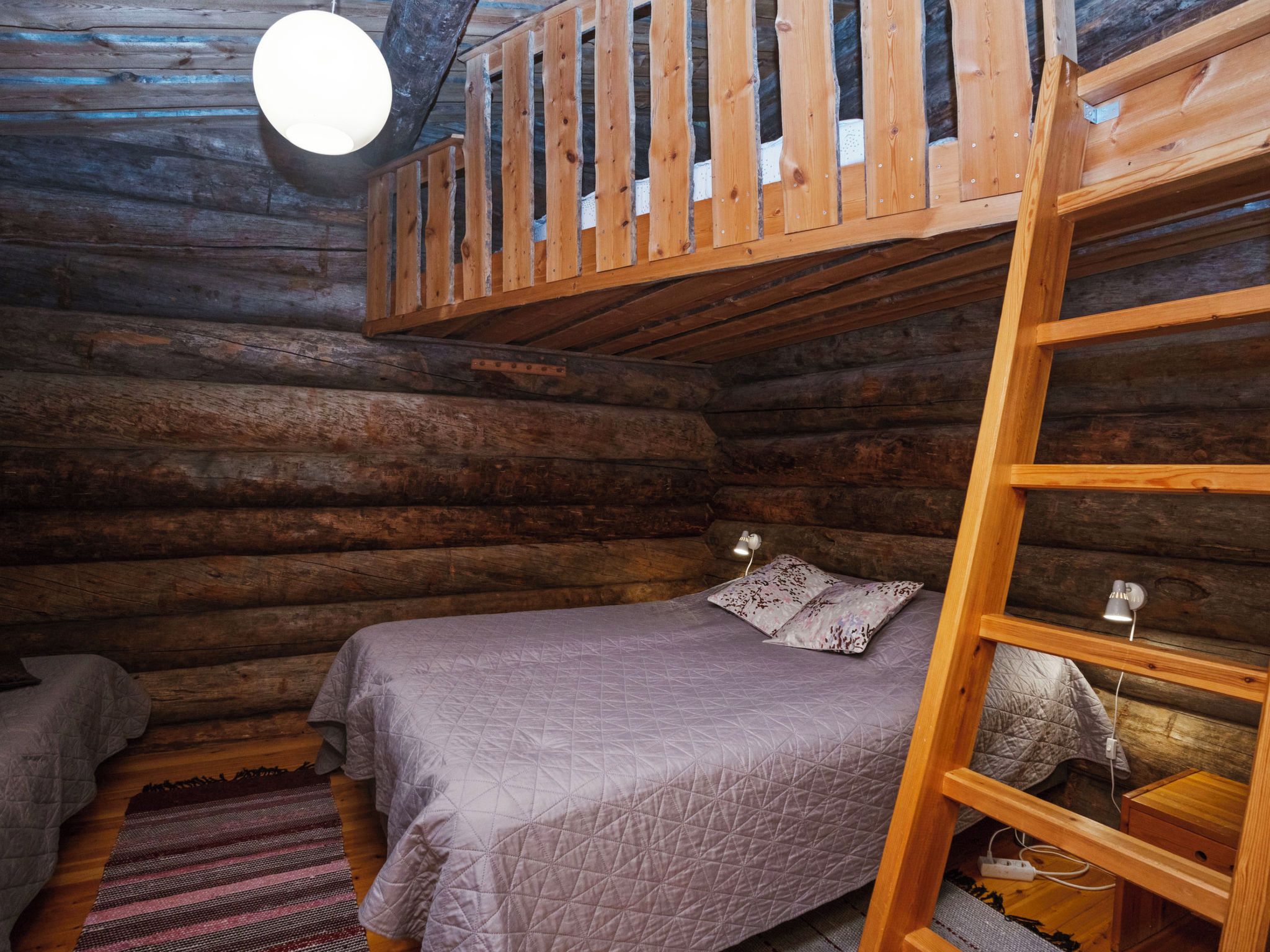 A log cabin room with a bunk bed, a small desk, and a hanging light fixture.