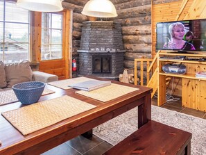 L’intérieur chaleureux d’un chalet avec une cheminée en pierre, un téléviseur et un coin repas agrémenté de sets de table.