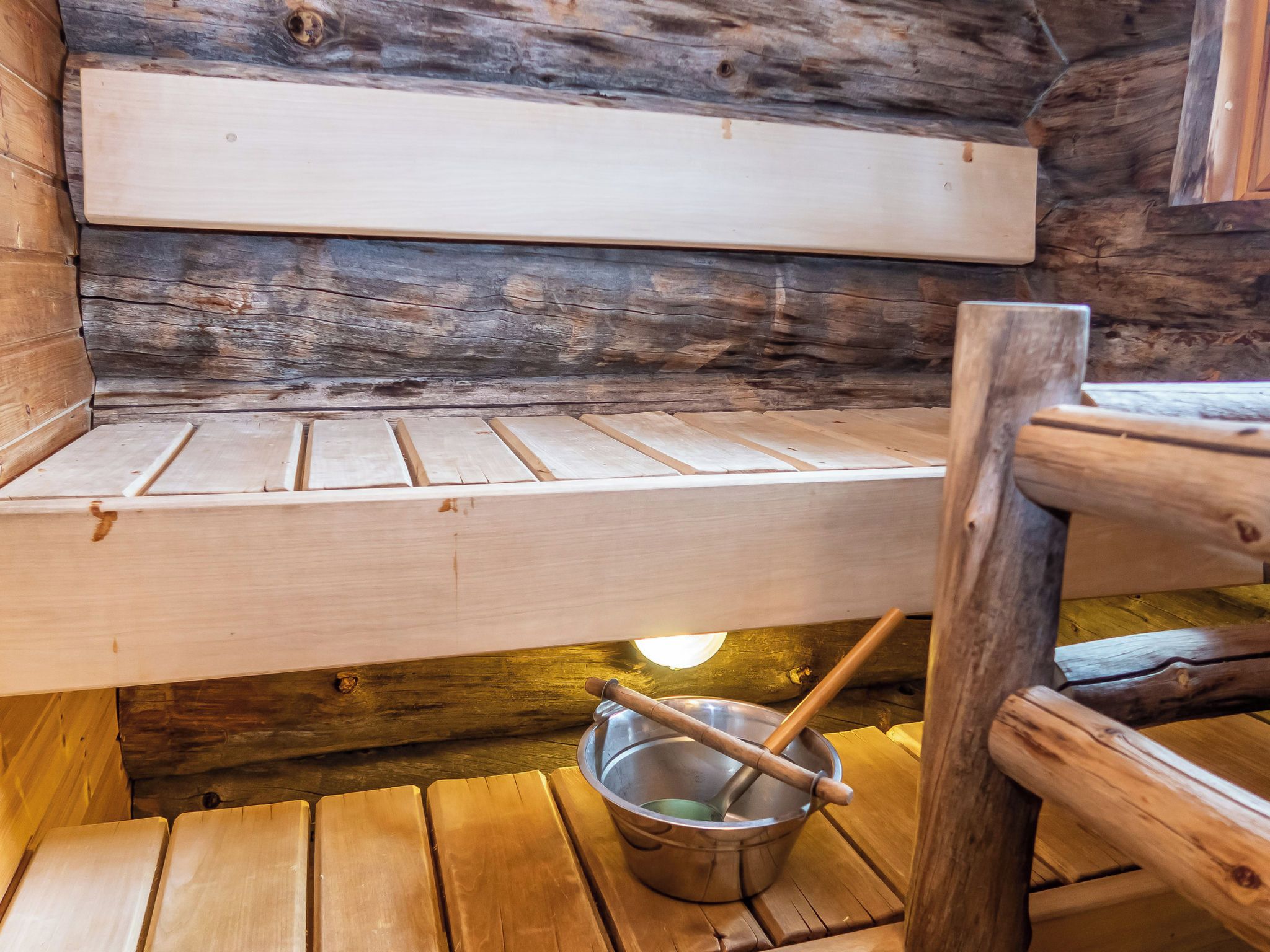A wooden bench with a metal bucket and a wooden spoon underneath.