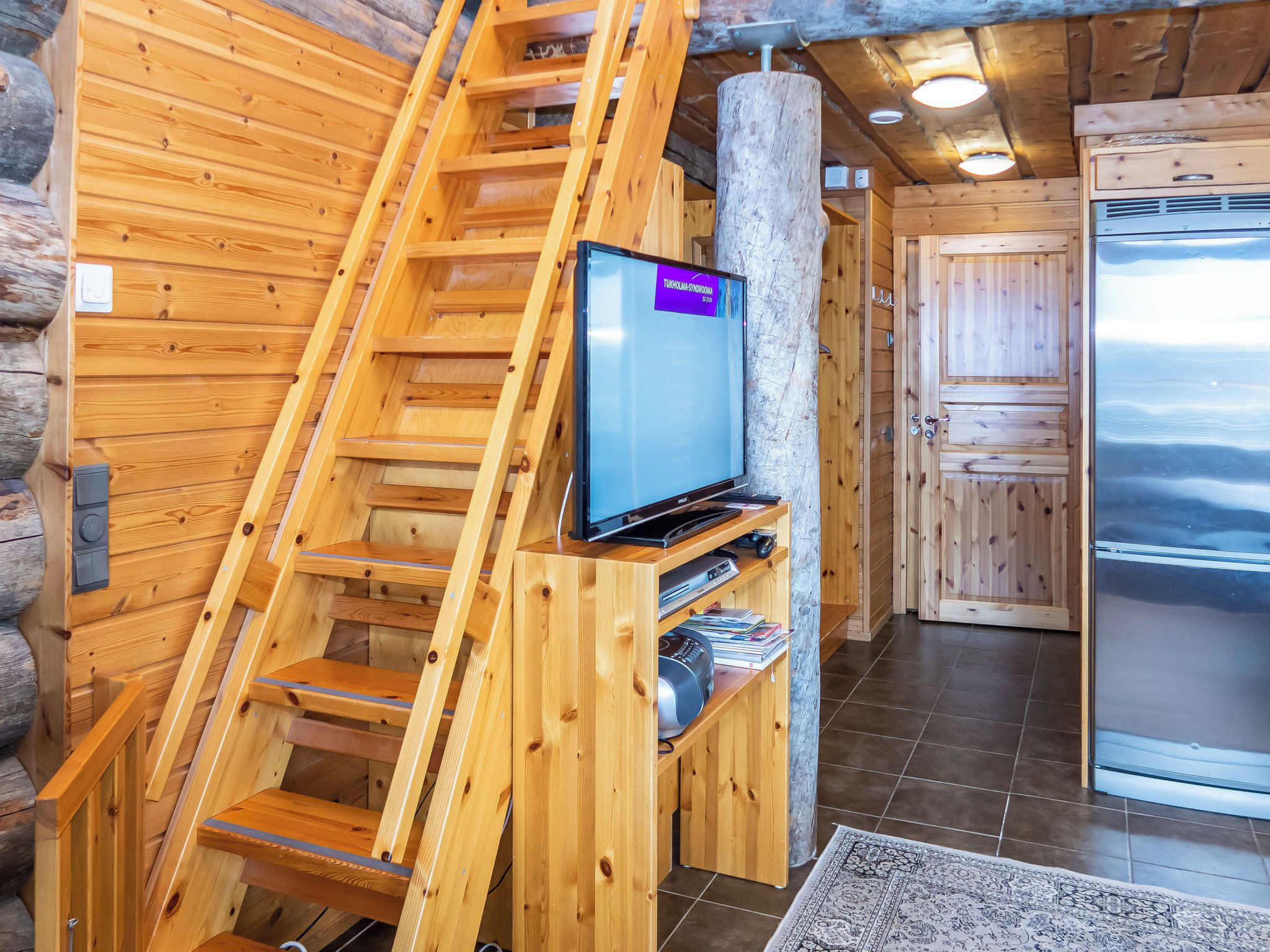 Ein Holzinnenraum mit einem an einer Holzkonstruktion befestigten Fernseher, einem Kühlschrank und einer Treppe.