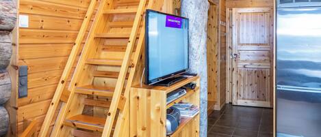 Ein Holzinnenraum mit einem an einer Holzkonstruktion befestigten Fernseher, einem Kühlschrank und einer Treppe.