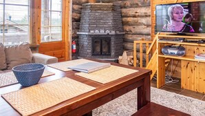 Ein gemütliches Blockhaus-Interieur mit Kamin aus Stein, einem Fernseher und einem Holztisch mit Untersetzern.