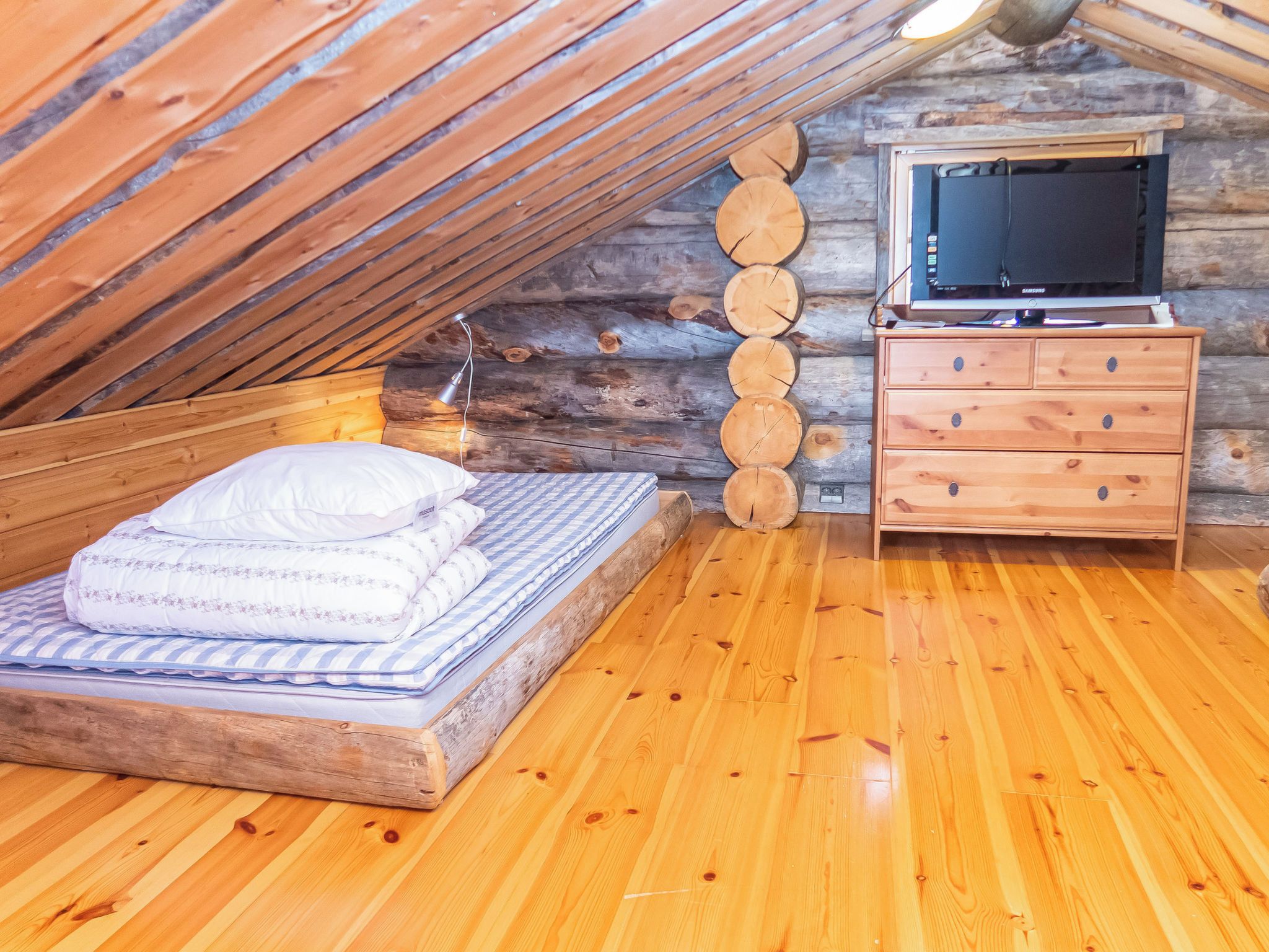 A cozy attic bedroom with a wooden bed, a dresser, and a television.