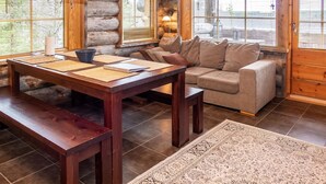 Ein gemütliches Blockhaus-Interieur mit einem Holzespeisetisch, gepolsterten Sitzmöglichkeiten und großen Fenstern.