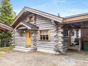 Een vakantiehuis in blokhutstijl, met een houten deur, een raam met luiken en een bordje waarop 'VILLA OLIVIA' staat.