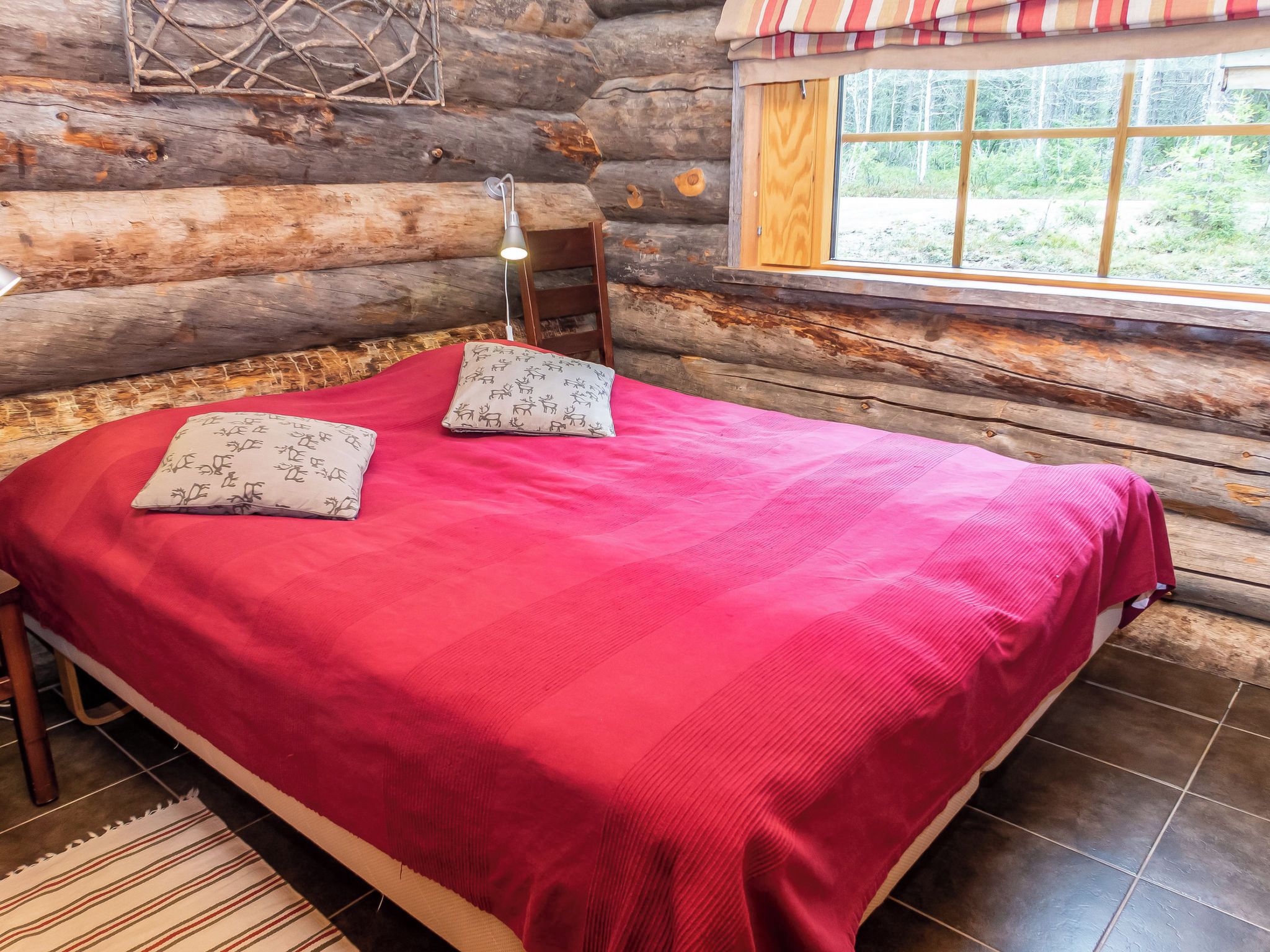 A log cabin bedroom with a bed, pillows, a window, and a view of the outdoors.