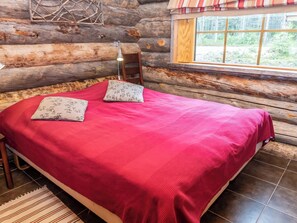 A log cabin bedroom with a bed, pillows, a window, and a view of the outdoors.
