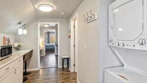 Ett tvättrum med en tvättmaskin och en torktumlare som man matar från framsidan, en mikrovågsugn och en liten pall.
