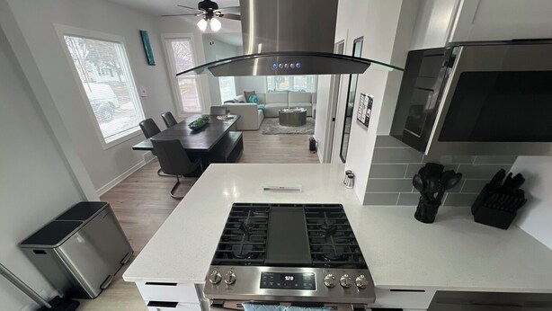 A modern kitchen with a central island, stainless steel appliances, and a dining area in the background.
