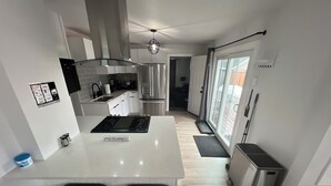 A modern kitchen with a central island, stainless steel appliances, and a sliding glass door leading to a balcony.