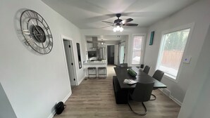 A modern kitchen with a ceiling fan, a dining area with a table and chairs, and a hallway leading to a living space.
