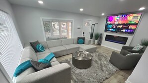 A modern living room with a grey sectional sofa, a round coffee table, and a flat-screen TV mounted on the wall.