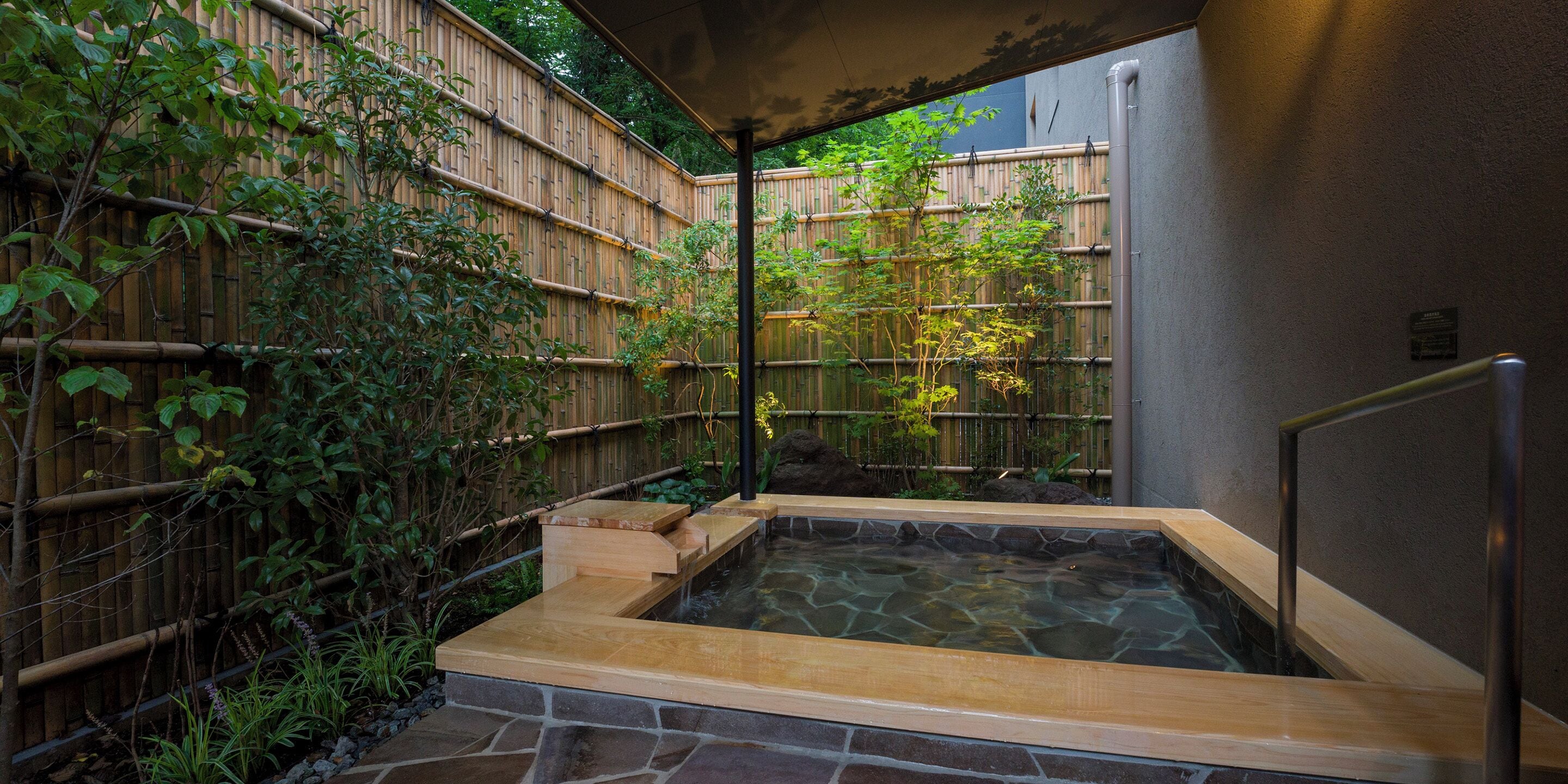 A hot spring area with a stone basin, bamboo fence, and a wooden deck.