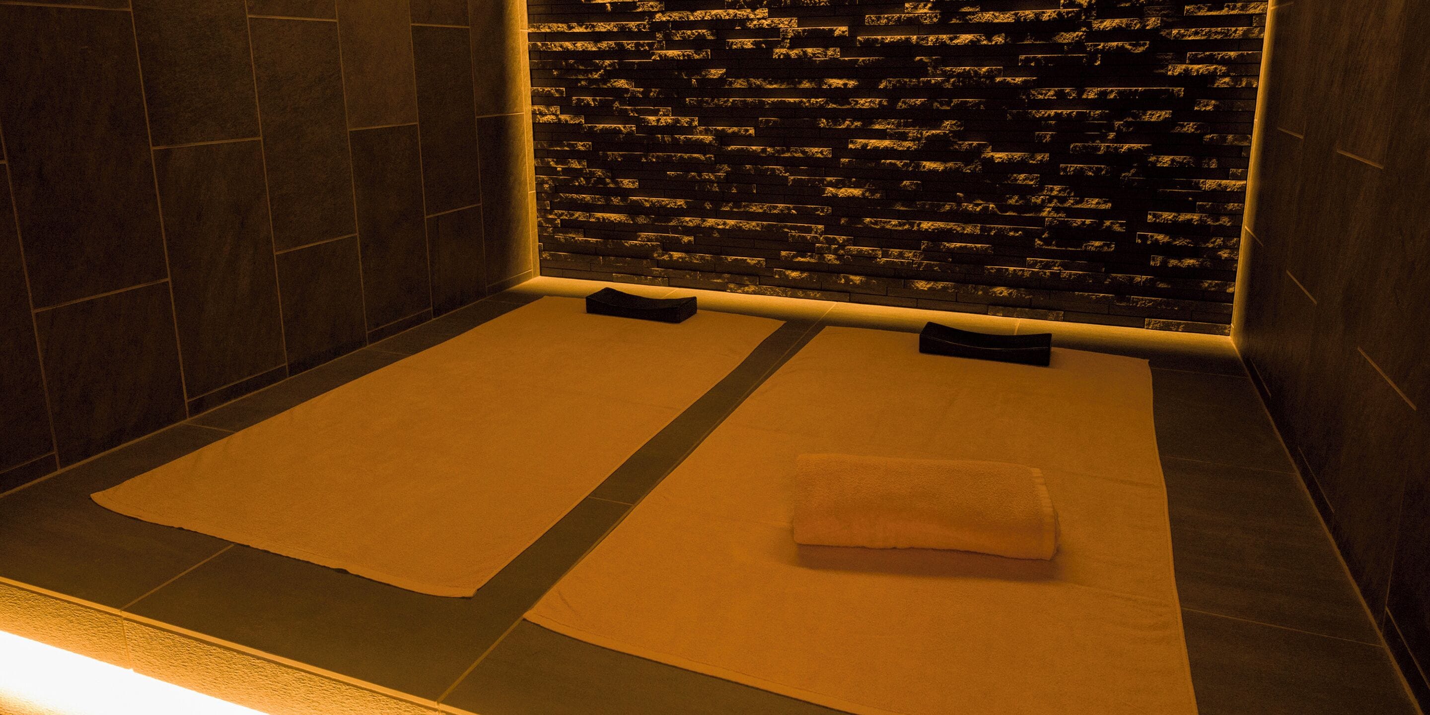 A spa room with two massage tables, a stone wall, and a tiled floor.