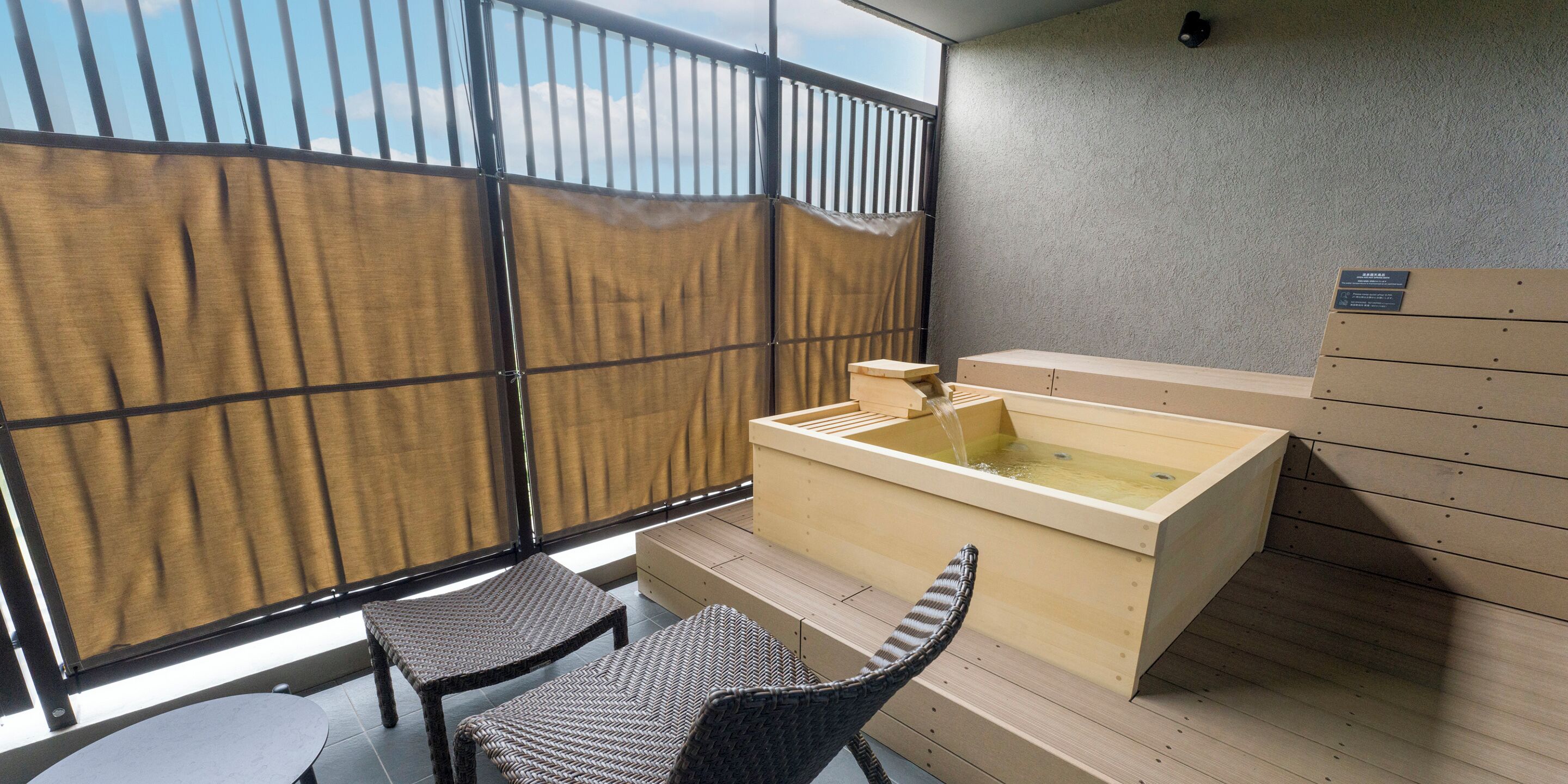 A room with a tatami mat floor, a wooden hot tub, and a sliding door with a view of the sky.