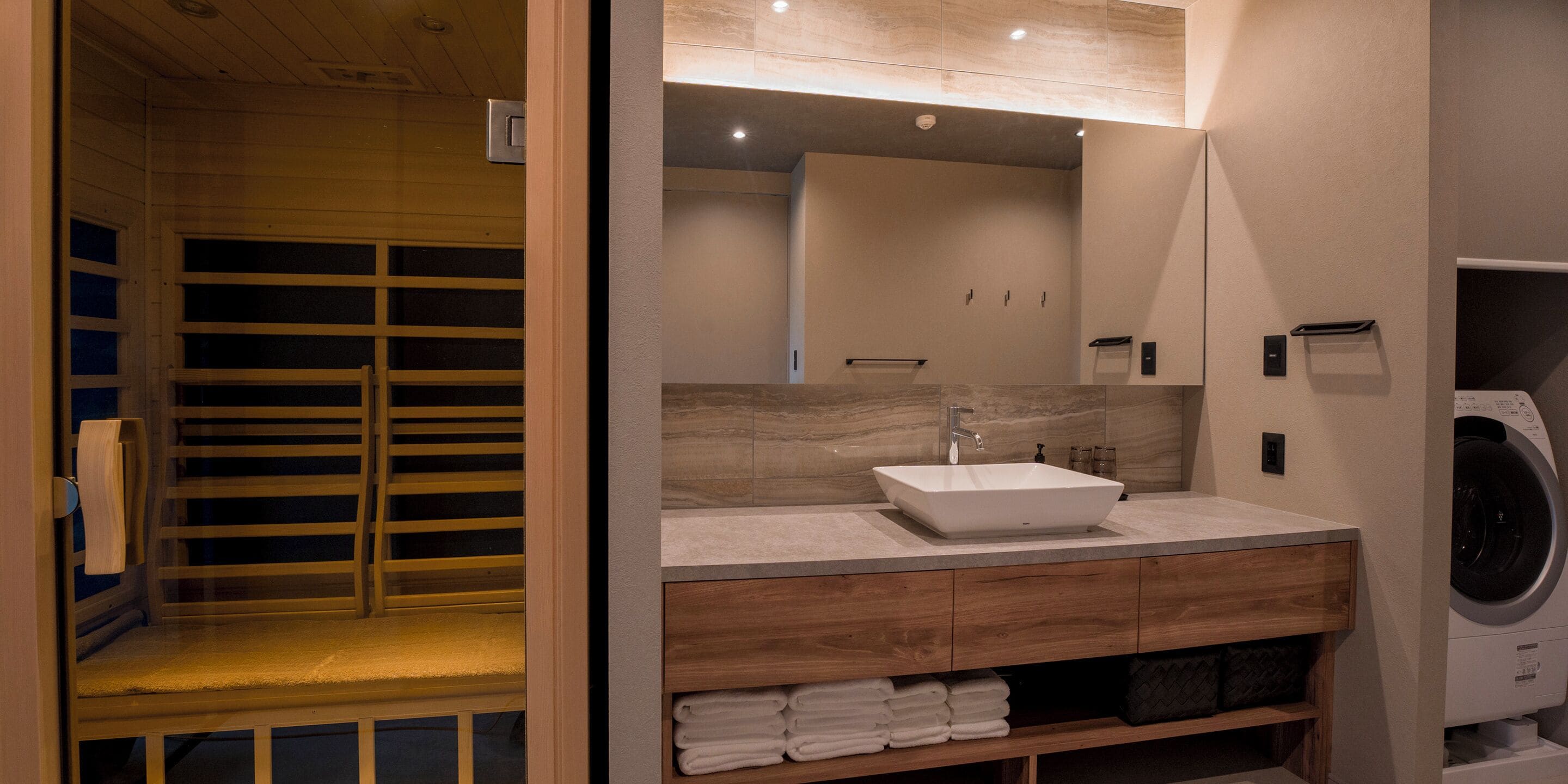 A modern bathroom with a wooden vanity, a large mirror, a built-in sink, and a washing machine.