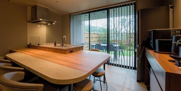Una cocina moderna con una isla grande, horno empotrado y puerta corredera de vidrio a un jardín trasero.