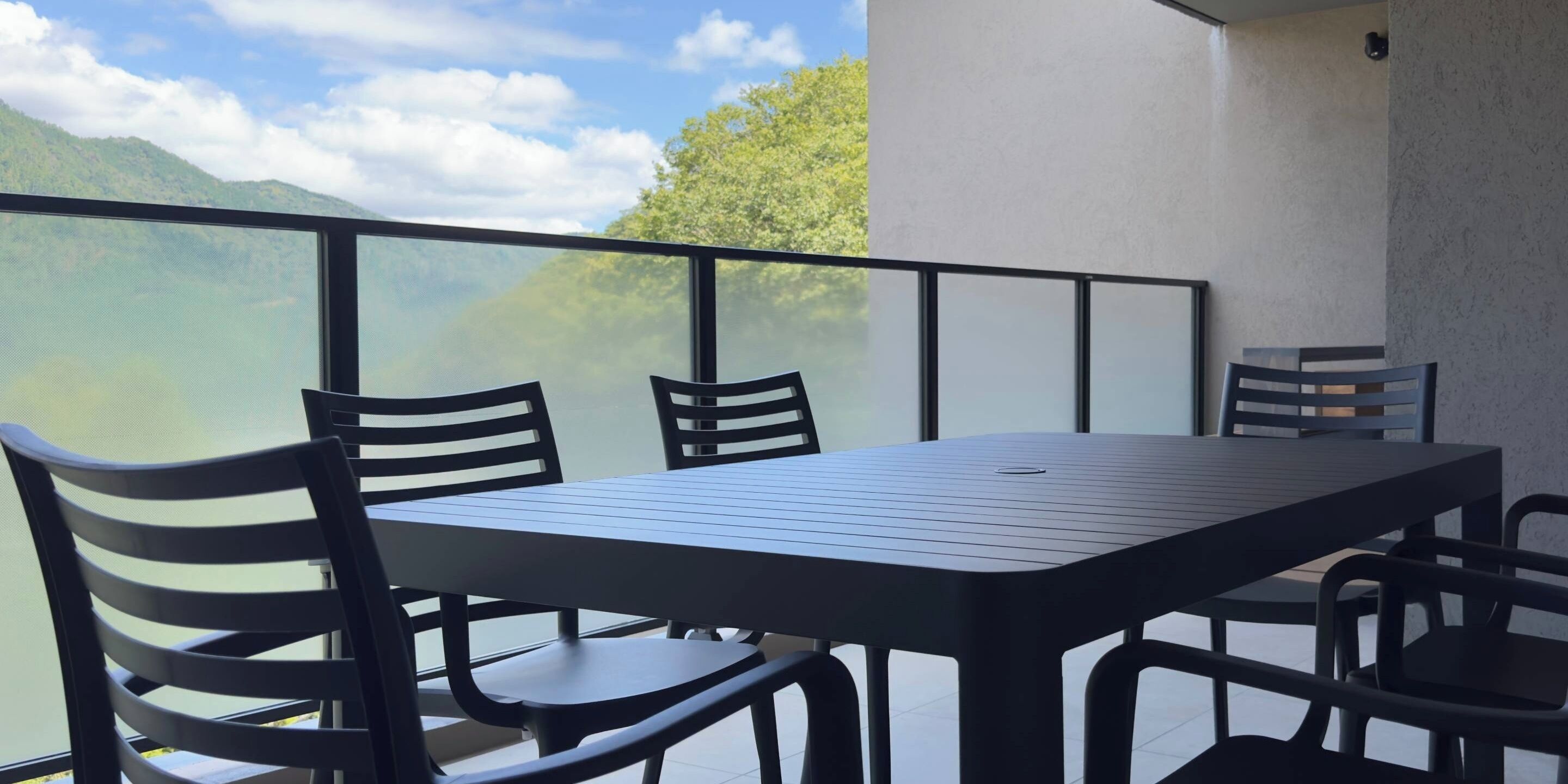 A balcony with a table and chairs, overlooking a mountainous landscape.