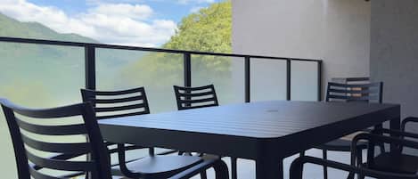 A balcony with a table and chairs, overlooking a mountainous landscape.