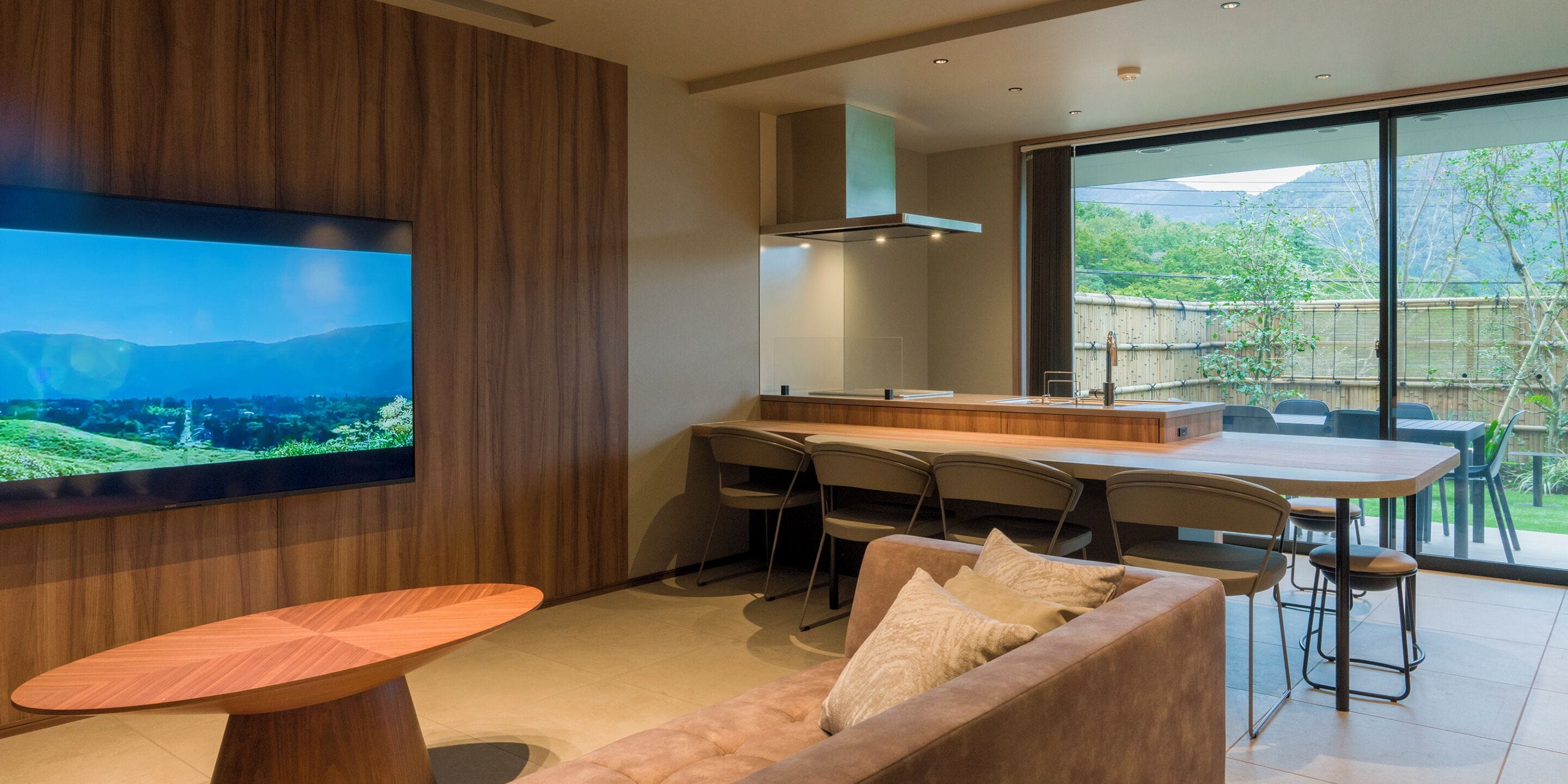 A modern kitchen with a large TV, wooden paneling, and a dining area with chairs and a table.