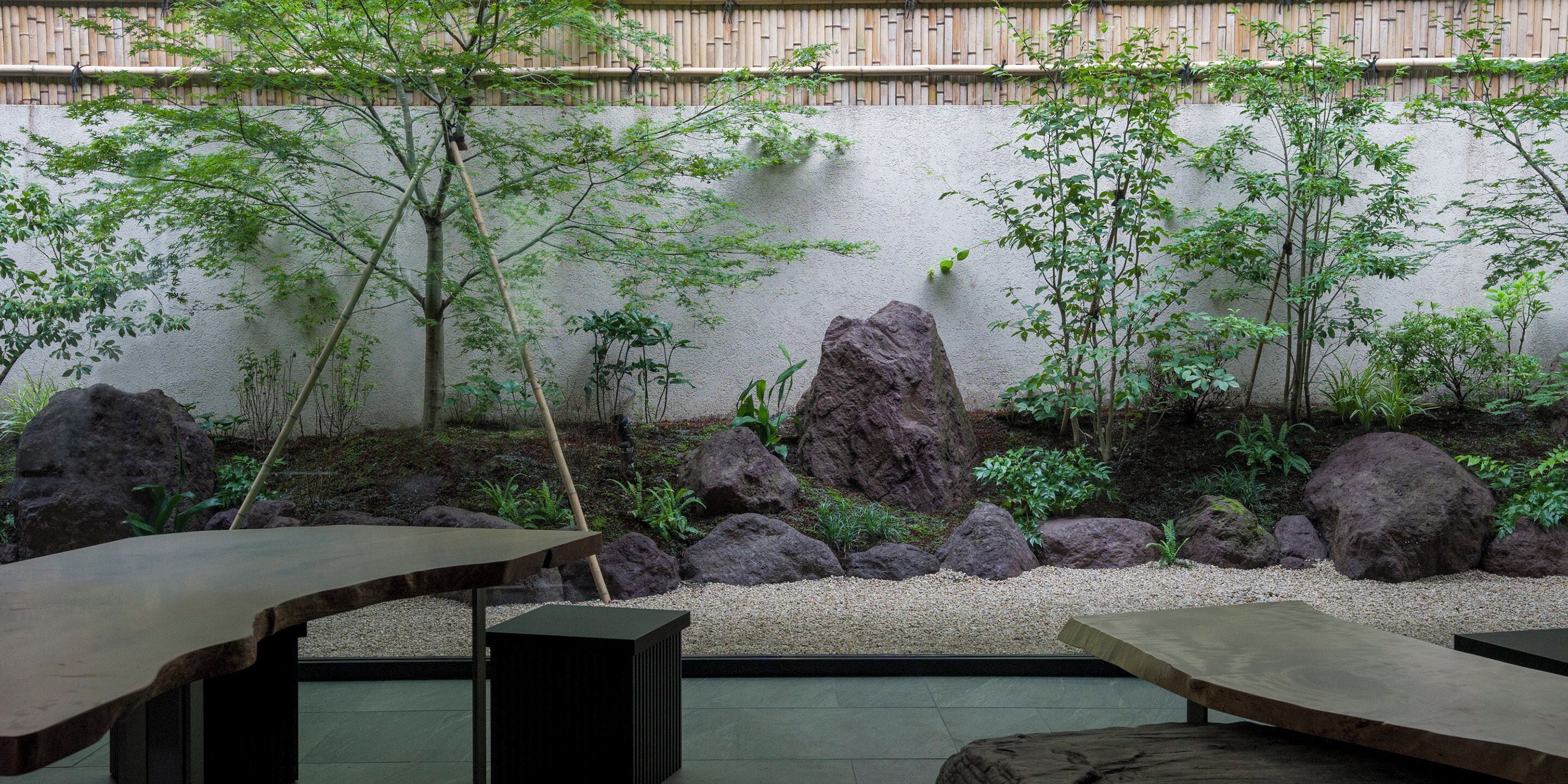 Un jardín tranquilo con una mesa y bancos de madera, rodeado de rocas y follaje.