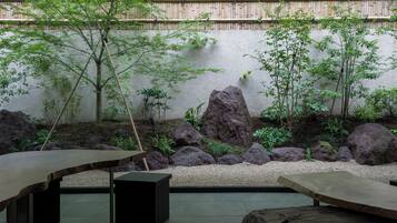 Un jardín tranquilo con una mesa y bancos de madera, rodeado de rocas y follaje.