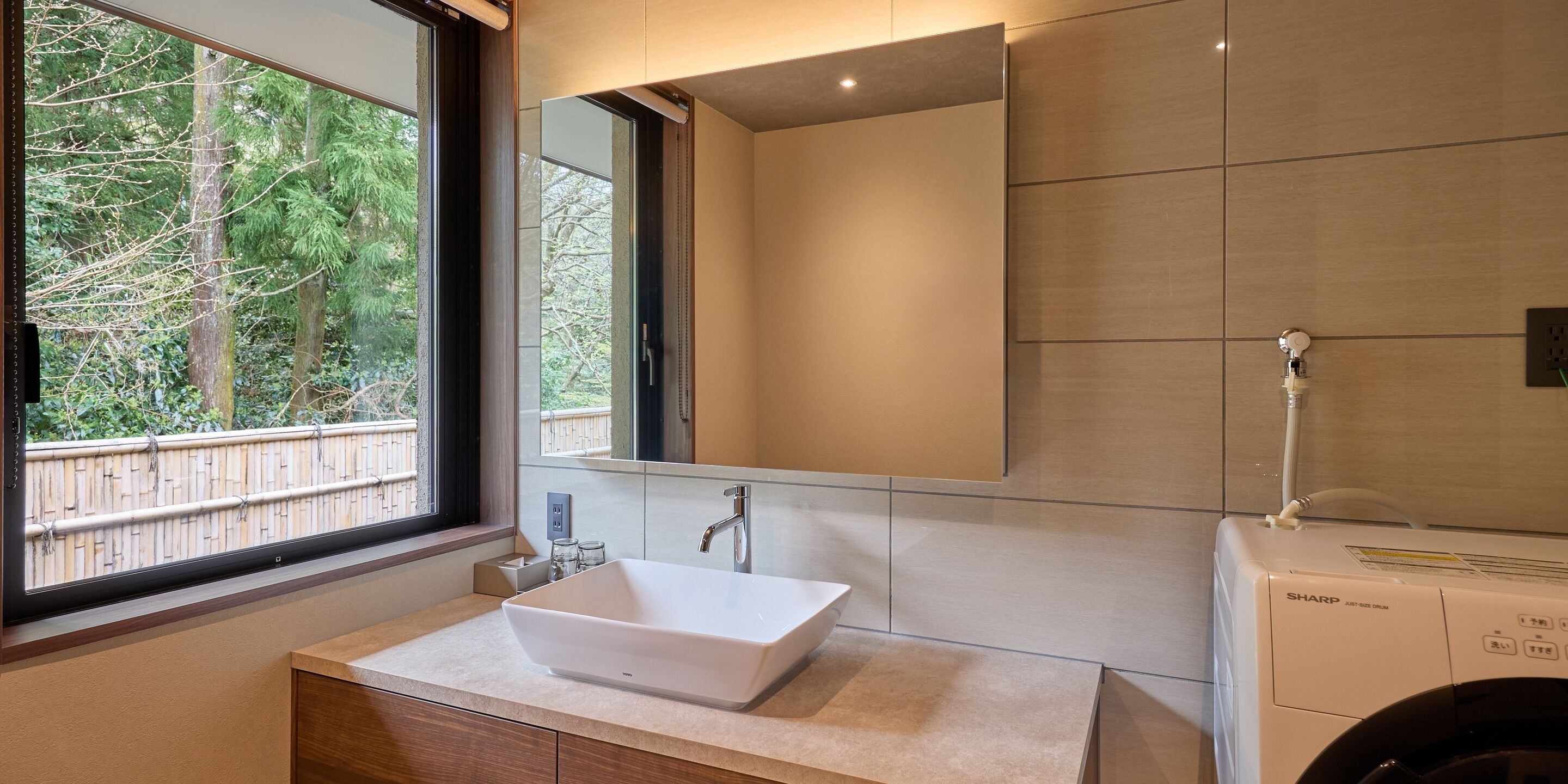 A modern bathroom with a large window, a white sink, and a mirror.