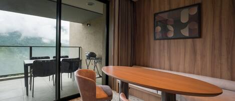 Un comedor moderno con una mesa y sillas de madera, un separador de vidrio y vistas al exterior.