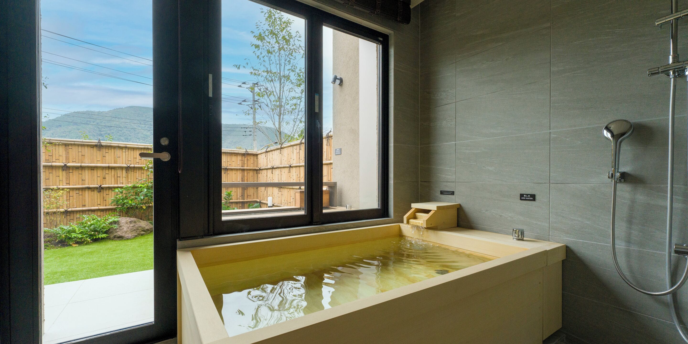 Un baño moderno con una bañera grande, ducha y ventana que ofrece vistas a un jardín trasero.