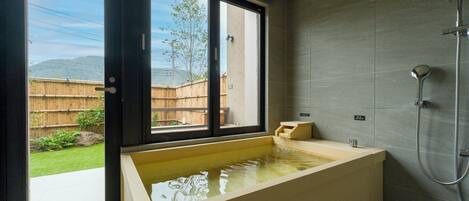 A modern bathroom with a large bathtub, a shower, and a window providing a view of a backyard.