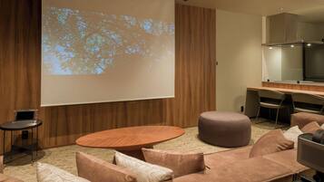 A modern conference room with a large projection screen, a round wooden table, and comfortable seating.